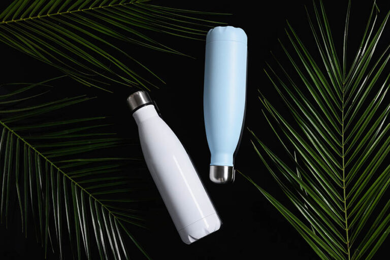 Thermo bottles and green leaves on black background, flat lay แก้วรักษ์โลก